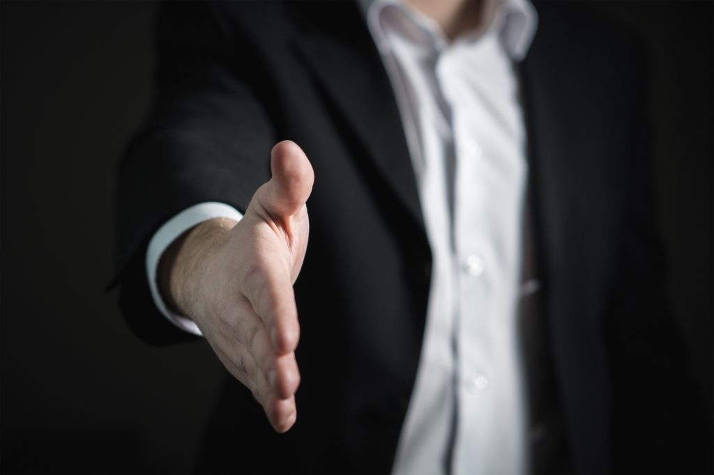 Point of view image of a suited man offering out his hand to shake as he offers you a graduate job, via your incredibal graduate engineering CV, because you have the right electronics career skills - an example would be networking for engineers.