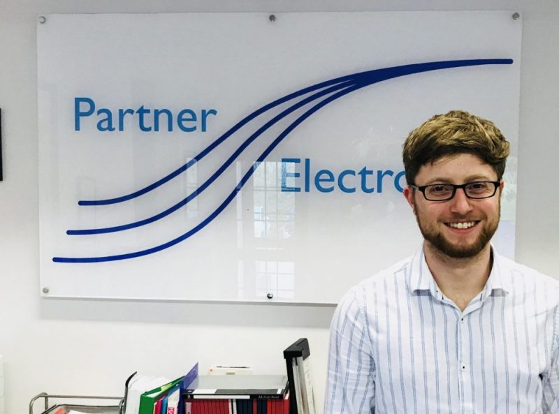 Pic of new graduate recruit Ryan Clark infront of our Partner Electronics sign
